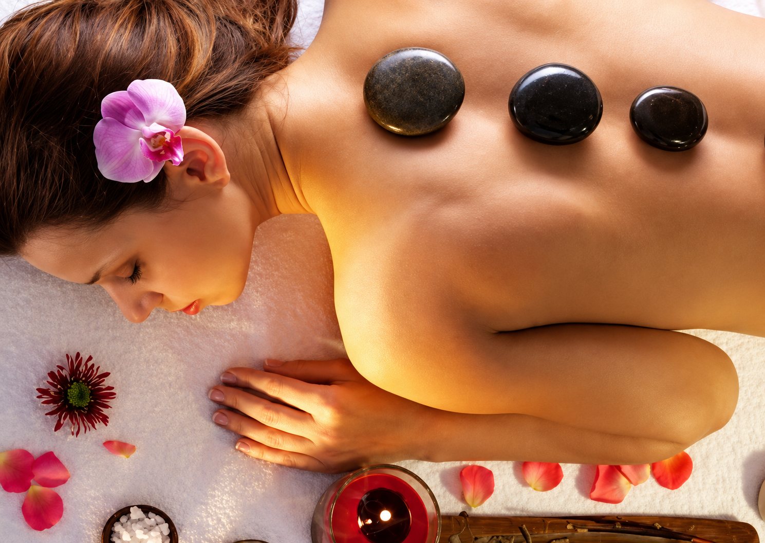 Femme allongée recevant un massage aux pierres chaudes, à la lueur d’une bougie